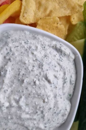 Picture of a bowl of cottage cheese with some dipping tortilla chips, cucumbers, lettuce leaves and bell peppers.