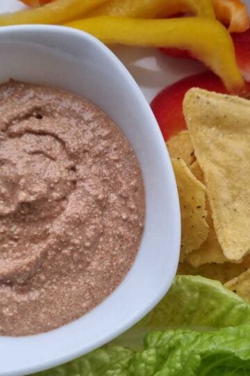 Picture of a bowl filled with cottage cheese taco dip with tortilla chips, lettuce, bell peppers.