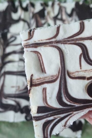 Hand holding a square piece of frozen cottage cheese bark decorated with swirled dark chocolate.