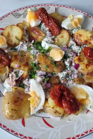 A plate of high protein crispy potato salad garnished with hard boiled eggs, sun dried tomatoes and chopped dill and parsley.