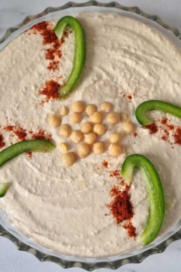 A plate of cottage cheese garnished with chickpeas in the middlem some green bell peppers and paprika.