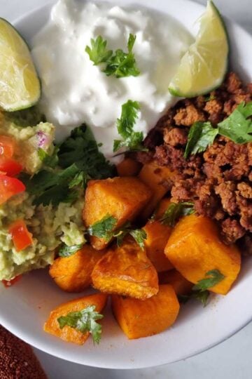 Cottage cheese sweet potato beef bowl garnished with lime wedges and chopped cilantro.