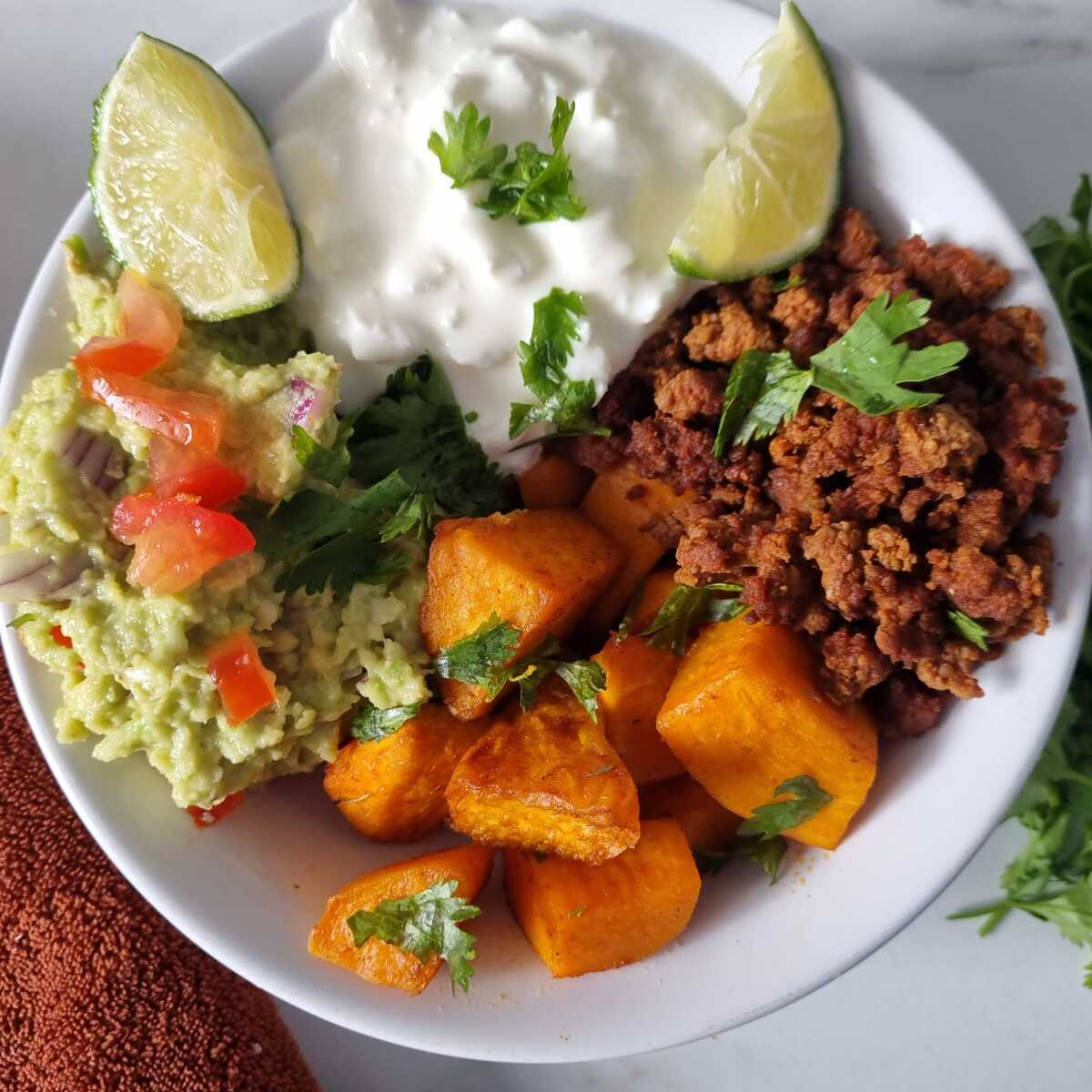 Viral cottage cheese sweet potato beef bowl garnished with wedges of lime and chopped cilantro.