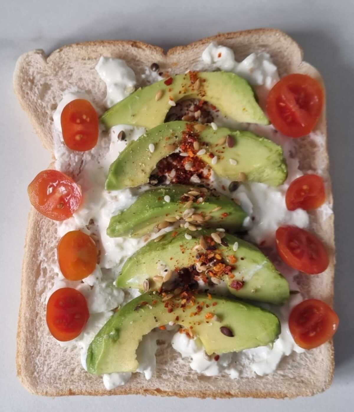 Toast with cotatge cheese and avocado garnished with halved cherry toamtoes and chilli flakes.