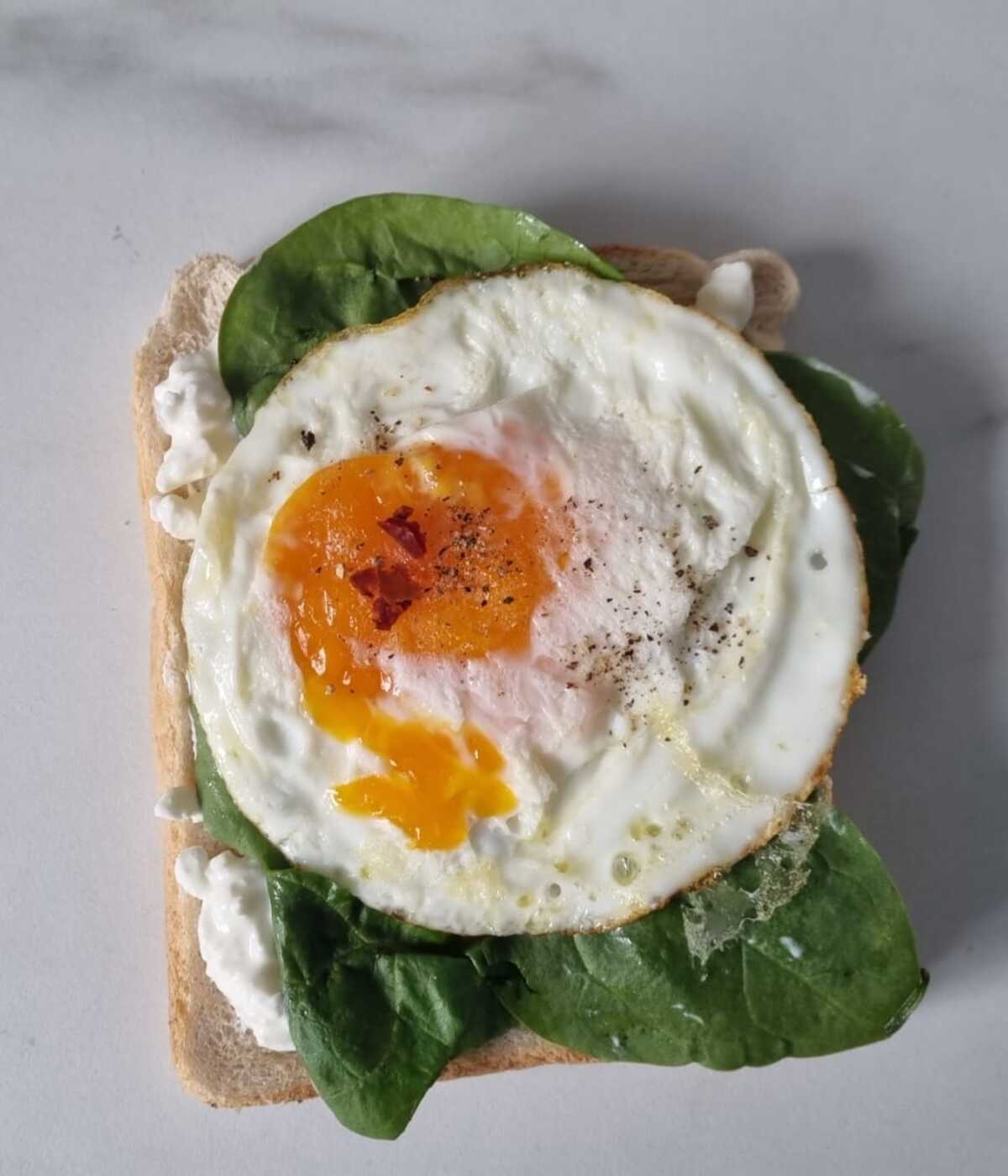 Cottage cheese spinach egg toast garnished with cracked black pepper and chilli flakes.