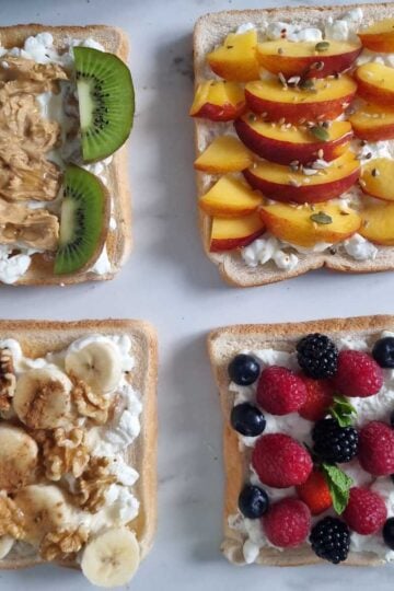 Four sweet cottage cheese toasts, one if them garnished with peanut butter and kiwi, one with peaches, one with banana dn walnuts and the last one with mixed berries.