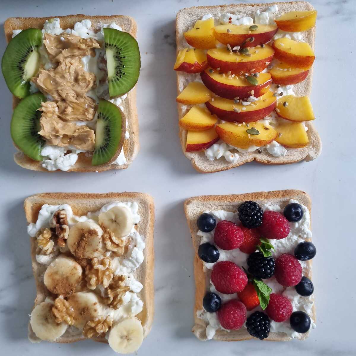 Four sweet cottage cheese toasts, one with peanut butter, one with peach, one with banana and the alst one with berries.
